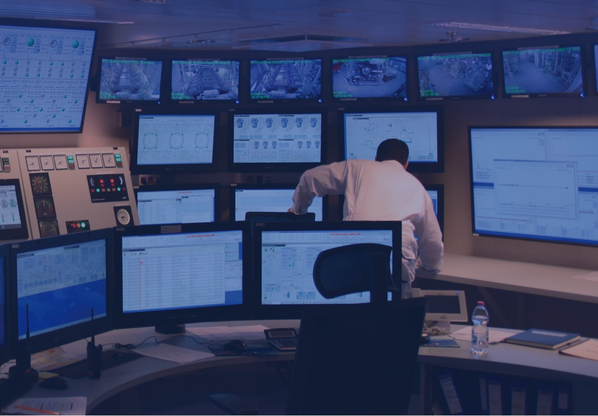 Control room with one employee overlooking many screens with blue lighting